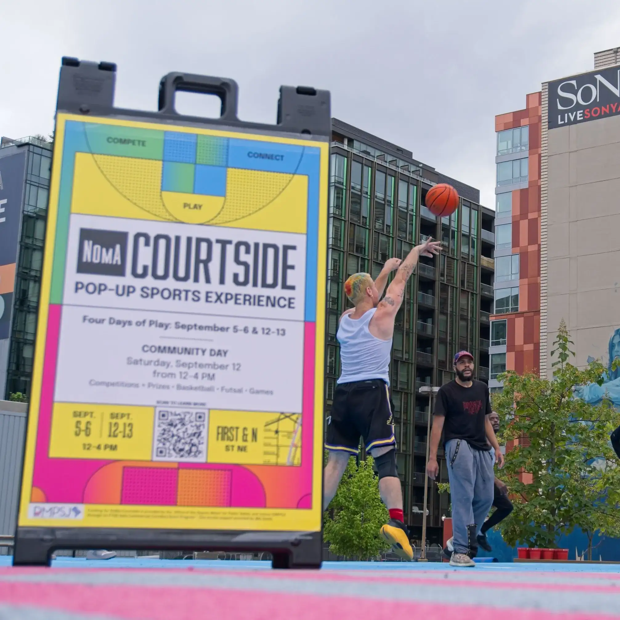 A player shoots on the pop-up court behind a colorful NoMa Courtside sign announcing four days of play